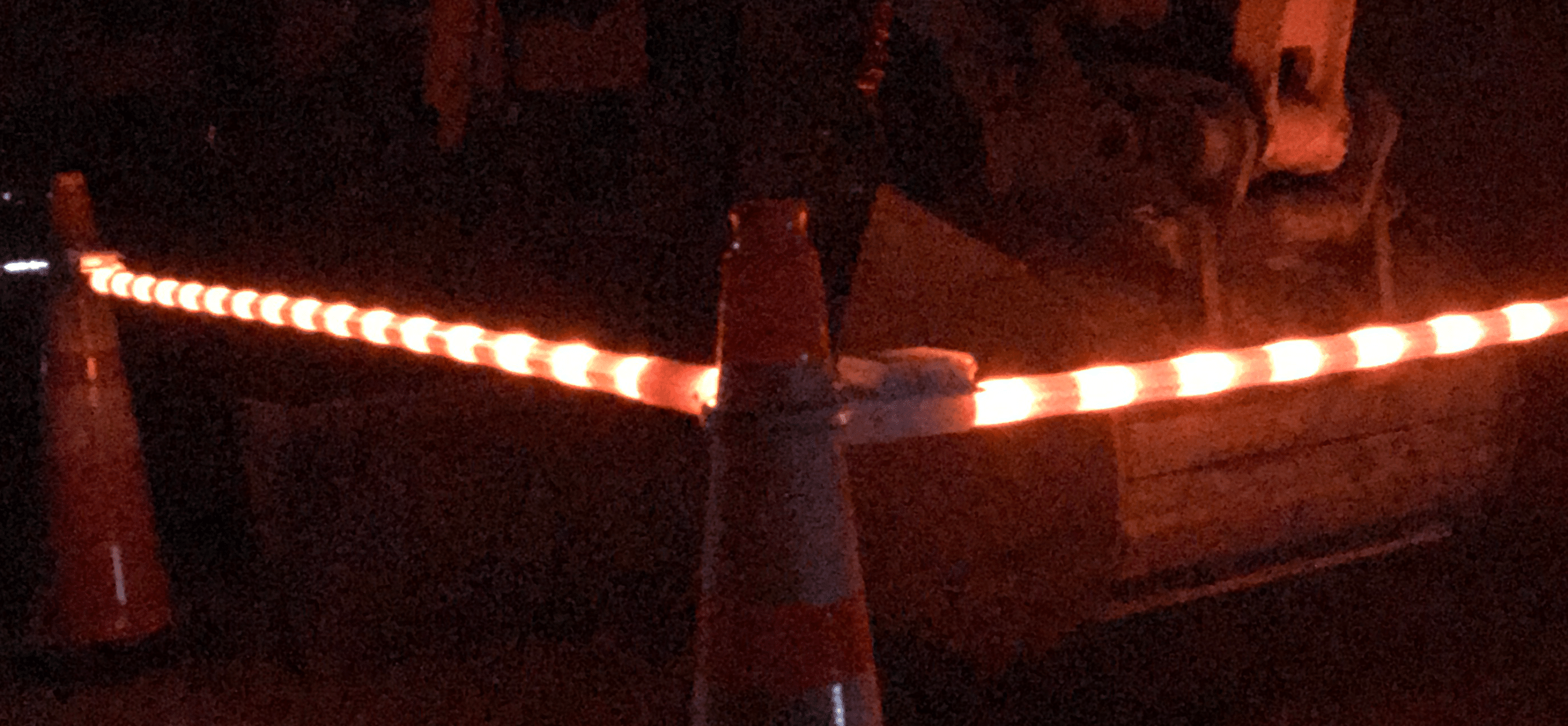 Illuminated safety cones connected by LED lights at a nighttime worksite, enhancing visibility and safety.